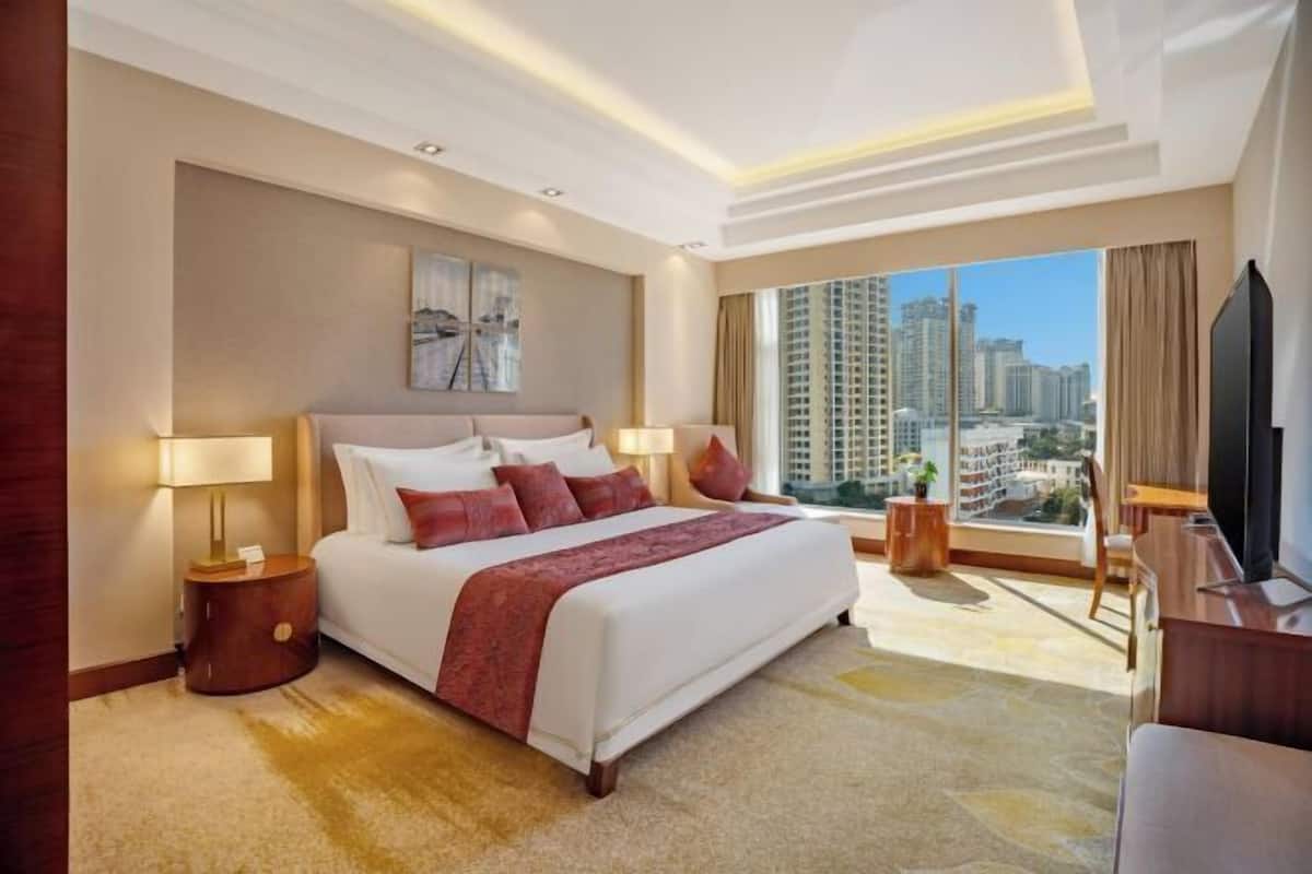 A hotel room with a large bed, a TV, a desk, and a view of tall buildings.