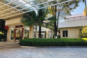 A hotel entrance with a glass canopy, palm trees, and a well-maintained hedge.