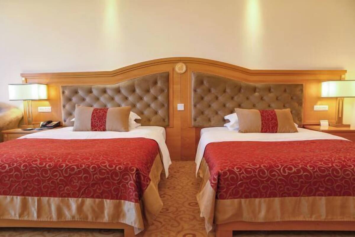 A hotel room with two beds, each with a tufted headboard and red patterned bedspreads.
