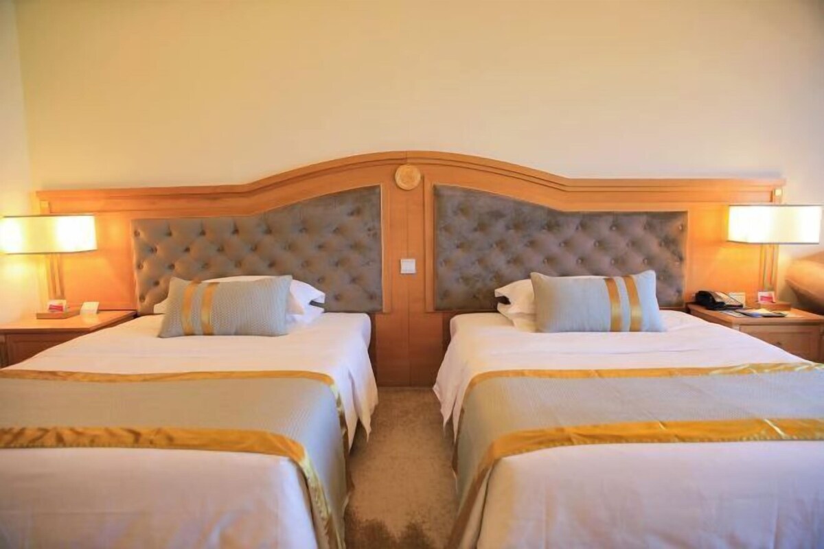 Habitación de hotel con dos camas, cabecera de madera y lámparas de noche.