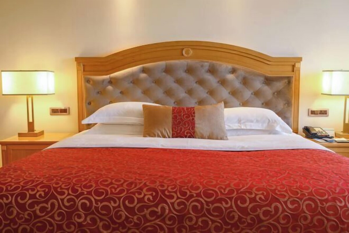 Una habitación de hotel con una cama grande, un cabecero capitonado y dos lámparas de noche.