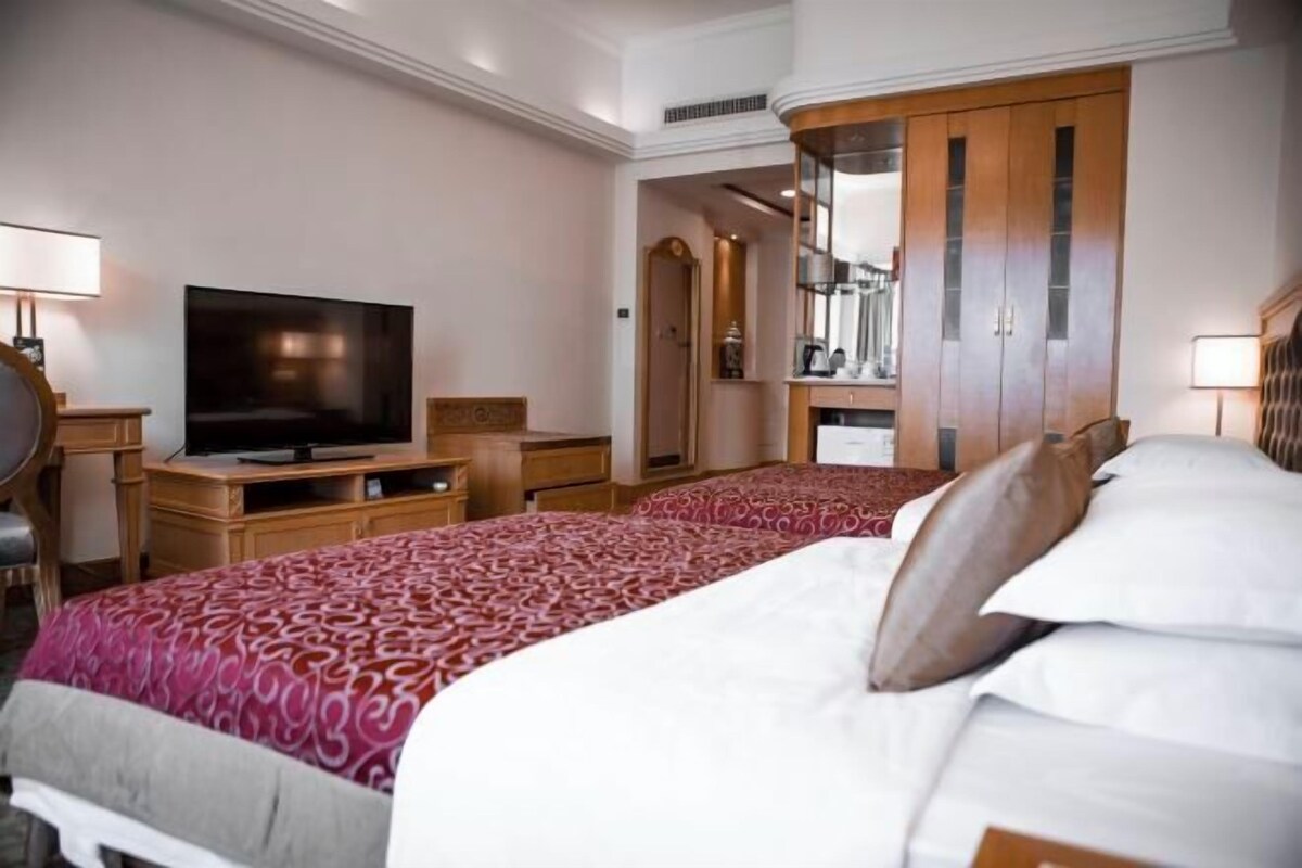 Una habitación de hotel con una cama grande, televisión, muebles de madera y un espejo.