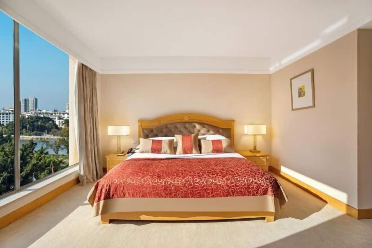 A hotel room with a large bed, two bedside tables, a view of a cityscape, and a window with curtains.