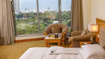 A hotel room with a large window, a bed, two armchairs, a small table with a tray, and a lamp.