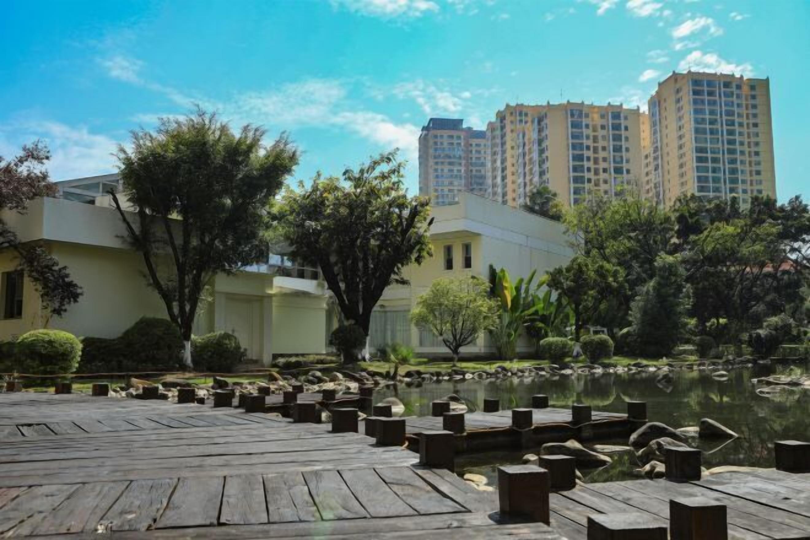 A serene courtyard with a wooden deck, a pond, and surrounding greenery.