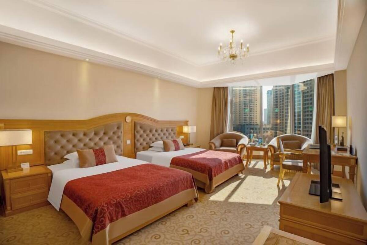 A hotel room with two beds, a TV, a desk, and a view of tall buildings.
