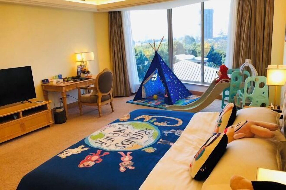 Habitación de hotel con cama, escritorio, silla, televisor, ventana con vistas y una zona de juegos tipo tienda de campaña.