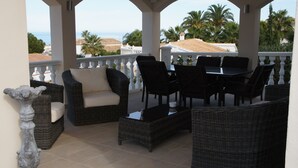 A covered outdoor seating area with wicker furniture, a white sofa, and a view of the beach and palm trees. - Quiet house and panoramic views  (Denia)