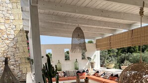 A covered outdoor seating area with stone walls, cactus plants, and a hanging woven light fixture. - House / Villa - Parabita (Parabita)