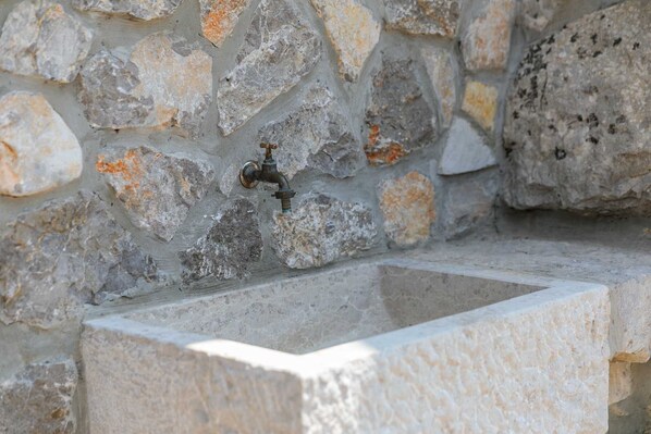 Un lavamanos de piedra con un grifo frente a una pared de piedra tosca.