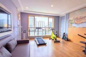 Een kamer met een loopband, een hometrainer en gewichten, grote ramen met uitzicht op de stad, en een bank.