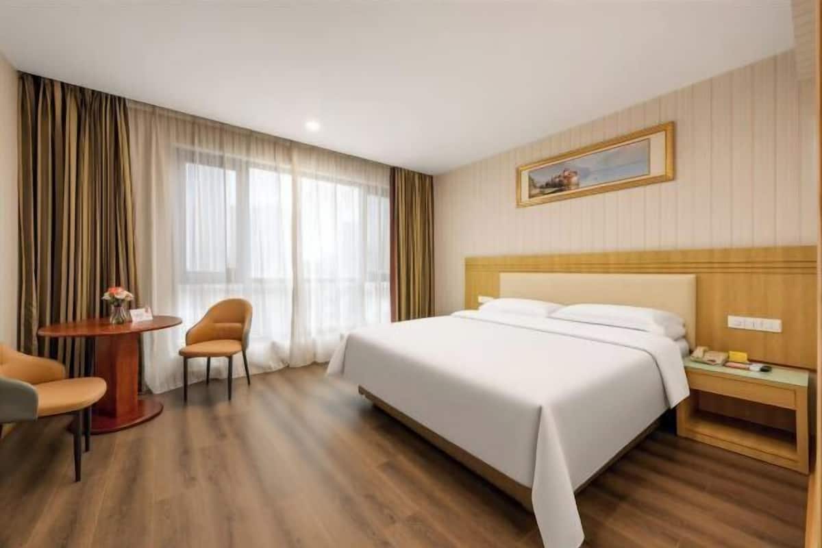 A hotel room with a bed, a round table with chairs, a nightstand, and a painting on the wall.