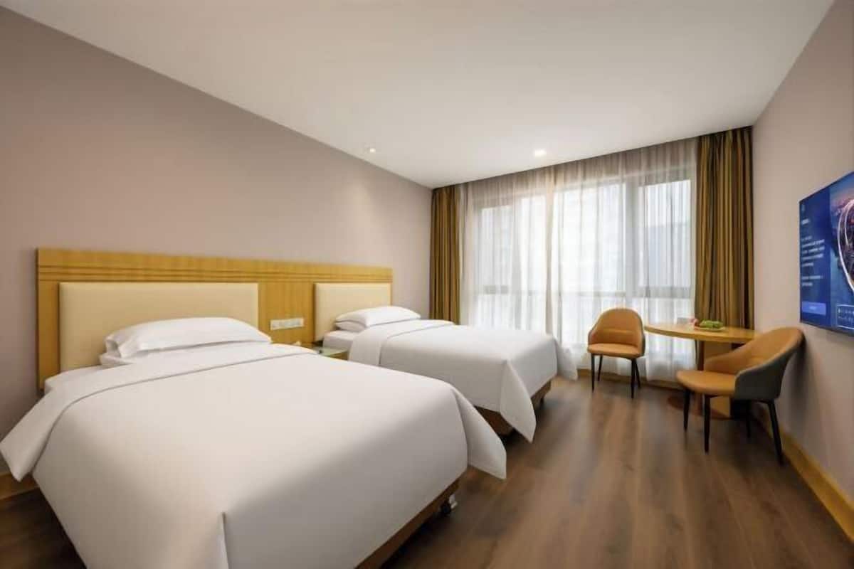A hotel room with two beds, a small table, and a chair.