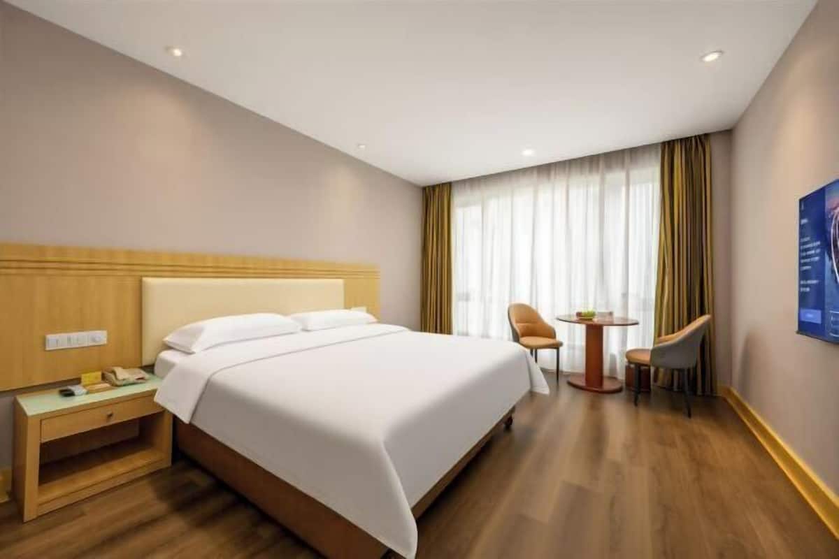 A hotel room with a bed, a nightstand, a chair, a small table, and a window with curtains.