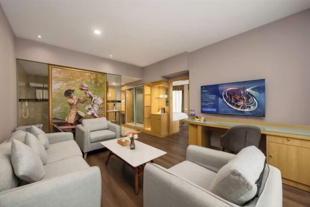 A modern hotel room with a sofa, armchairs, a coffee table, a desk, and a large painting on the wall.