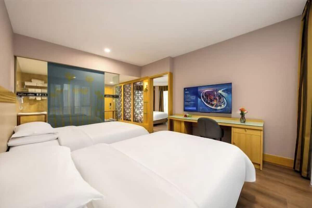 A hotel room with two beds, a desk, a computer, and a large mirror.