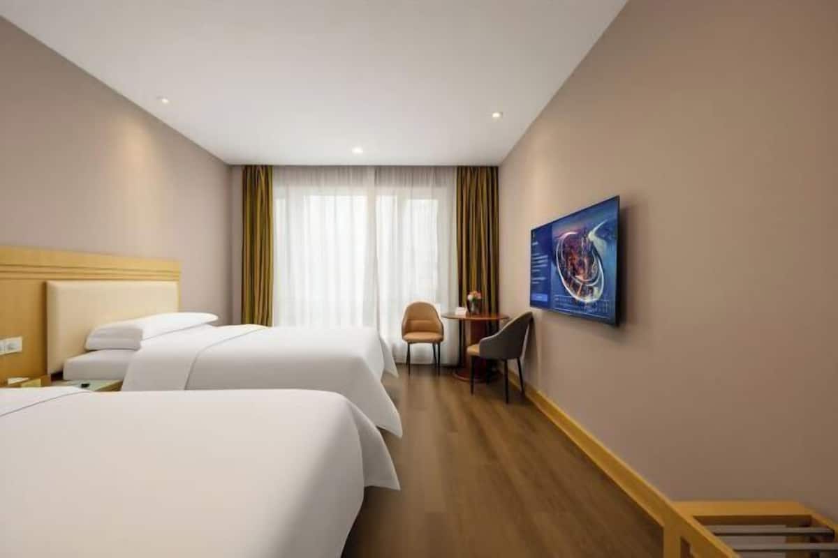 A hotel room with two beds, a desk, a chair, and a large window with curtains.