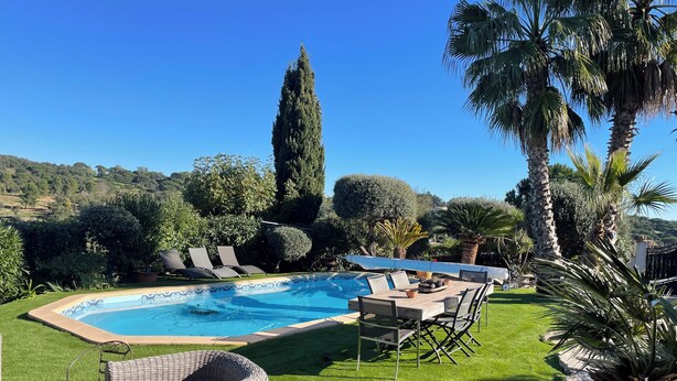 A swimming pool with lounge chairs and a table, surrounded by well-maintained grass and various trees.