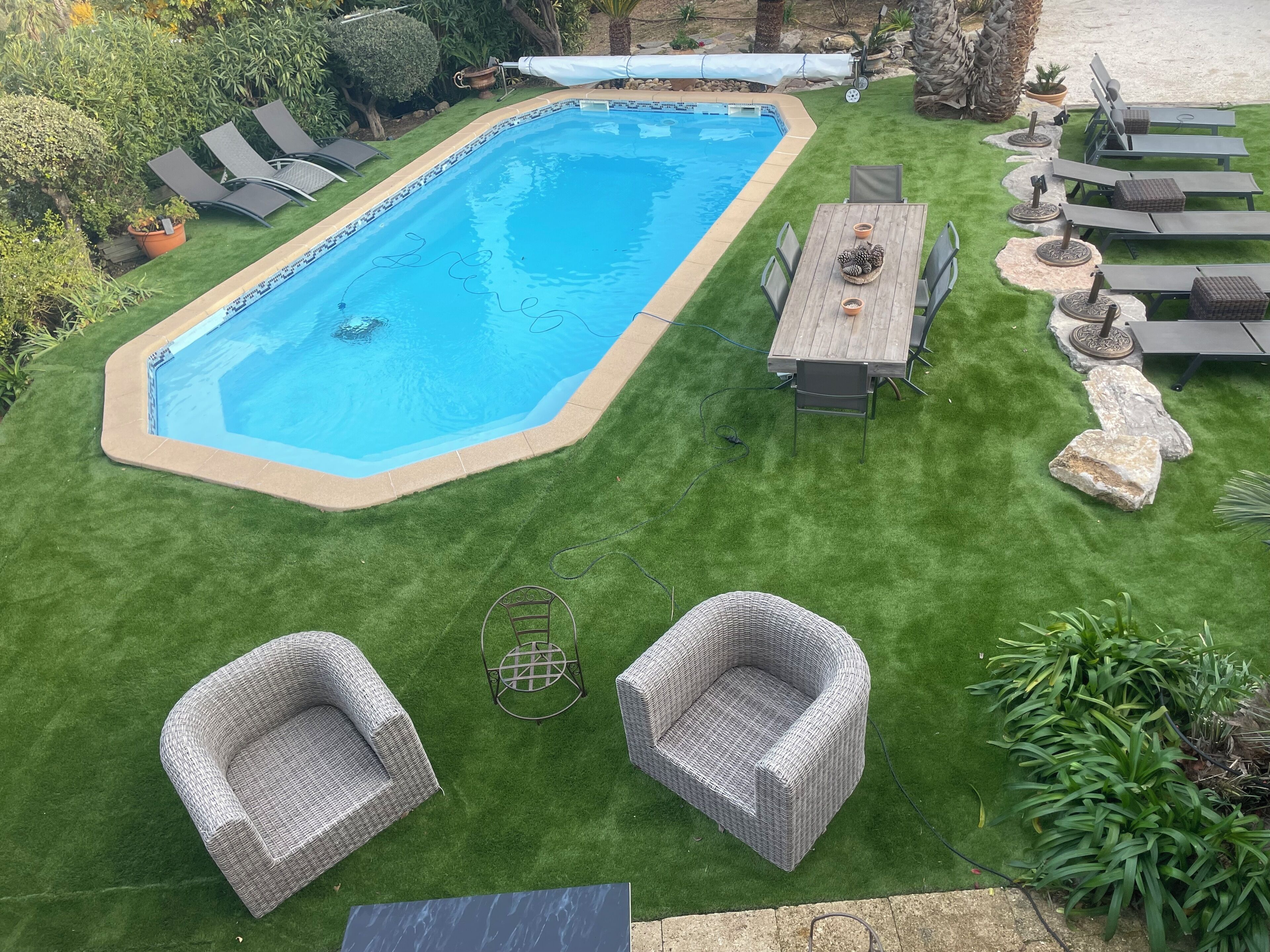 A rectangular swimming pool with a tiled edge, surrounded by a well-maintained lawn and outdoor furniture including lounge chairs and a table.
