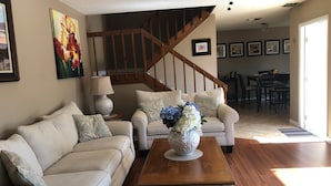 A living room with a sofa, a coffee table, and a vase of flowers. There is a staircase in the background leading to another room. - All inclusive, 2 bed 2 bath, pool, perfect location!  (Fort Myers)