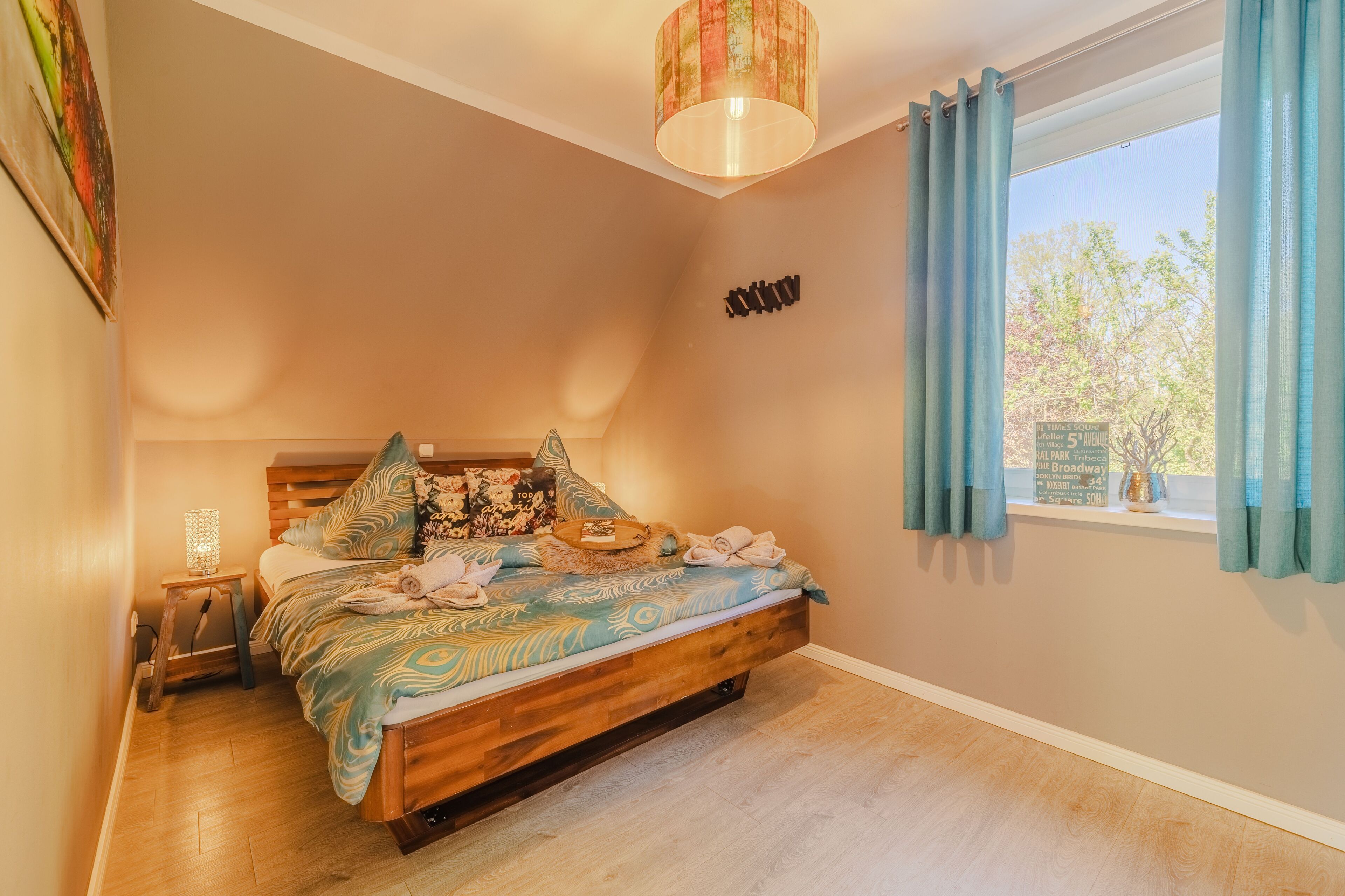 A bedroom with a wooden bed, a nightstand, a lamp, and a view of a park through a window.