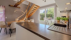 A modern kitchen with a wooden staircase, a large island with a sink, and a dining area with chairs. - Vacation home Hünzingen № 1 (Walsrode)
