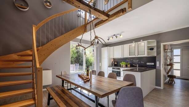 A modern kitchen with white cabinets, a wooden dining table, and a built-in bench. - Vacation home Hünzingen № 1 (Walsrode)