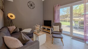 A modern living room with a grey sofa, a coffee table, a TV stand, and a large window with curtains. - Vacation home Hünzingen № 1 (Walsrode)