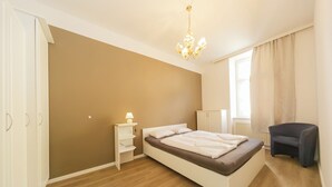 Une chambre à coucher comprenant un lit, une table de chevet, une lampe, une armoire, une chaise et un lustre.