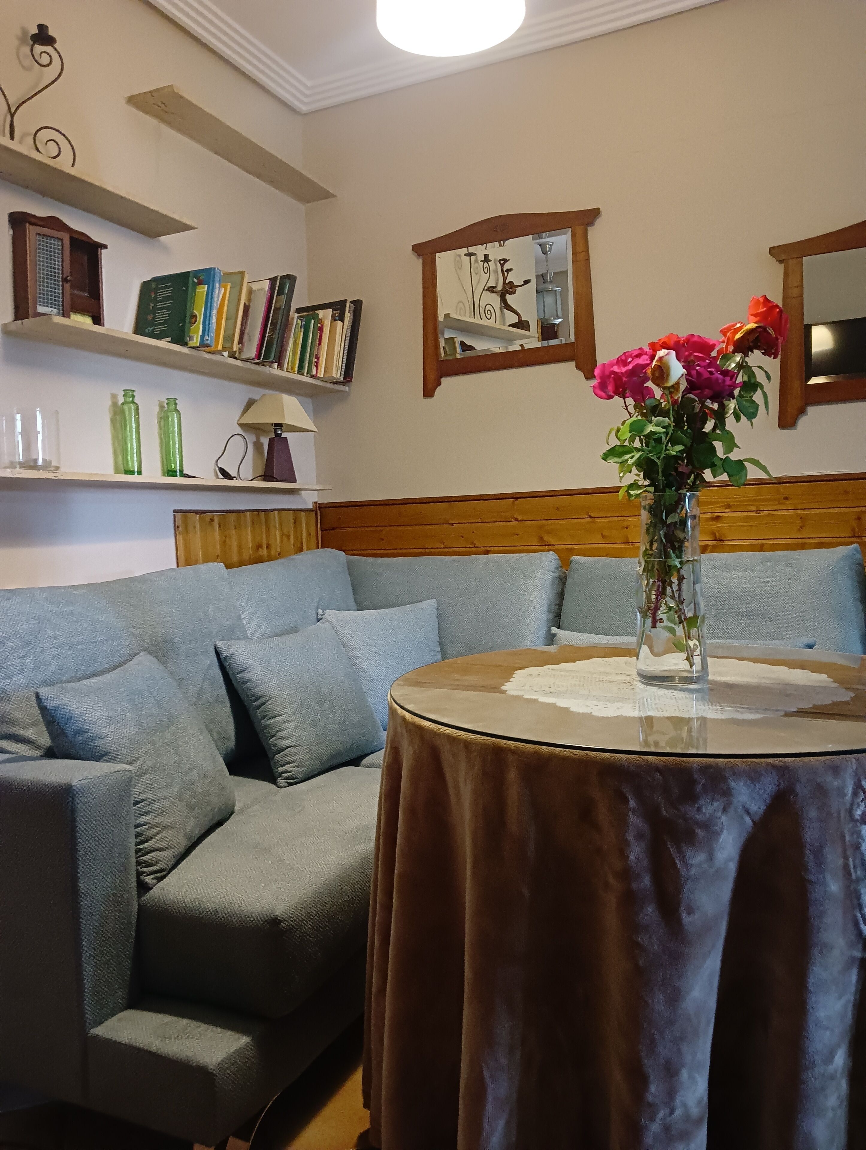Ein Wohnzimmer mit einer Couch, einem runden Tisch mit Blumenvase und Bücherregalen mit Büchern und Dekoration.