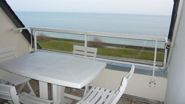 A balcony with a white table and chairs, overlooking a grassy area and the sea. - Apartment with access and stunning sea views (Damgan)