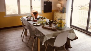 Ein Essbereich mit Tisch, gedeckten Plätzen, einer Blumenvase und Blick ins Freie durch ein Fenster.