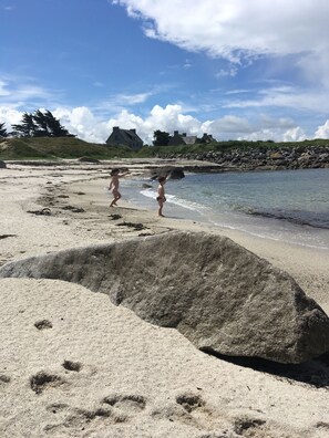 A sandy beach with footprints, a rocky shoreline, and houses in the background. - The sea at your feet in Brittany! (Plouescat)