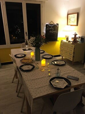 A dining table set for four with candles, a vase of flowers, and plates. - The sea at your feet in Brittany! (Plouescat)