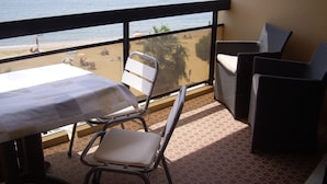 A balcony with a table and chairs, overlooking a beach with people and a sailboat. - APARTMENT IN SAINTE MAXIME (Sainte-Maxime)