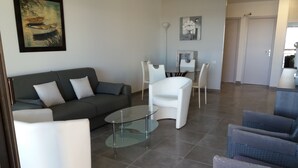 A modern living room with a grey sofa, white armchairs, a glass coffee table, and a dining area with white chairs. - APARTMENT IN SAINTE MAXIME (Sainte-Maxime)