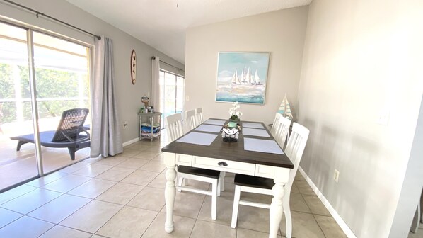 A dining area with a table and chairs, a painting on the wall, and a view of the outdoors.
