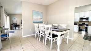 A dining area with a table and chairs, a kitchen with appliances, and a painting on the wall.