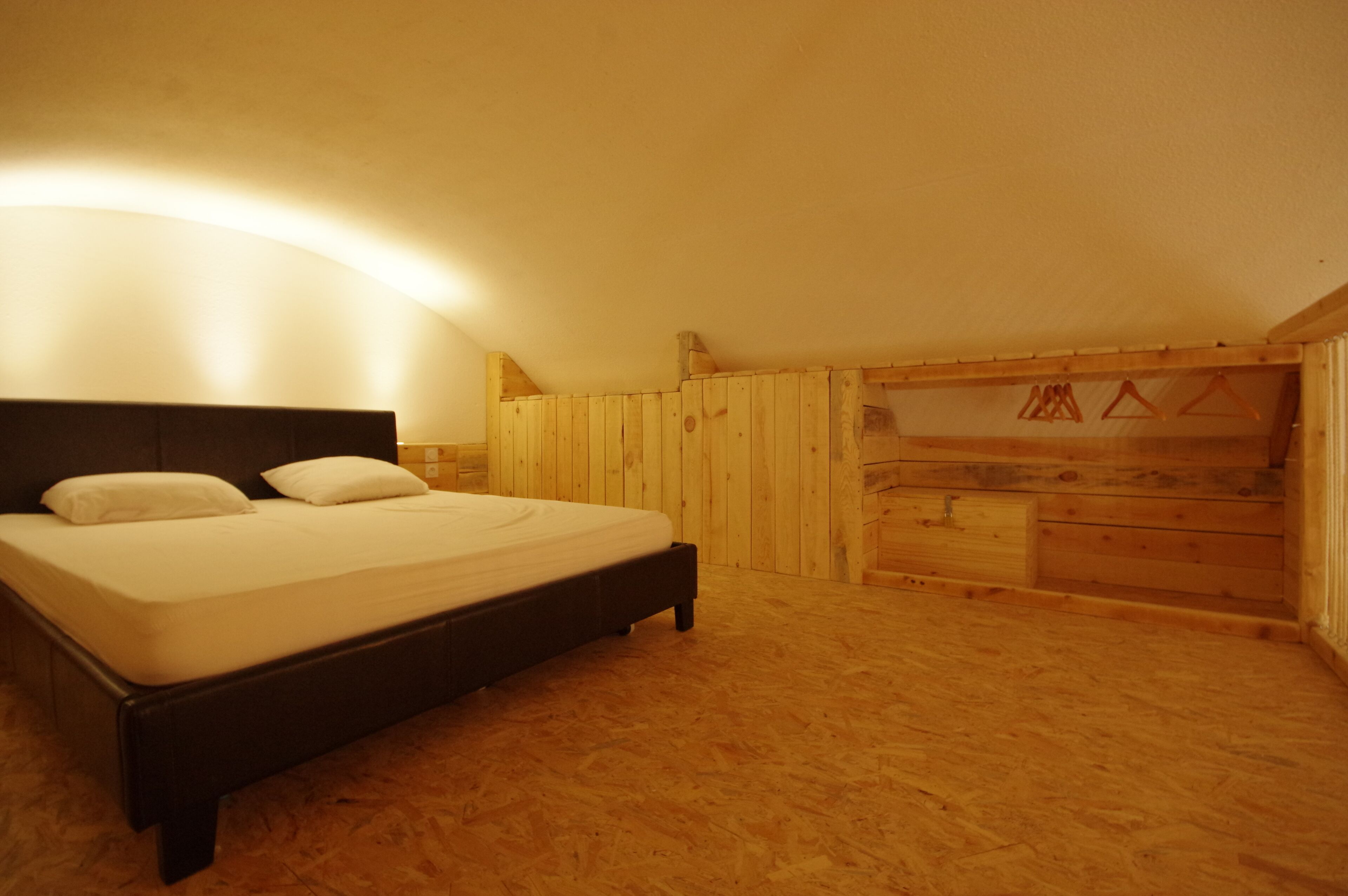A bedroom with a wooden floor, a bed with white bedding, and a sloped ceiling with wooden paneling.