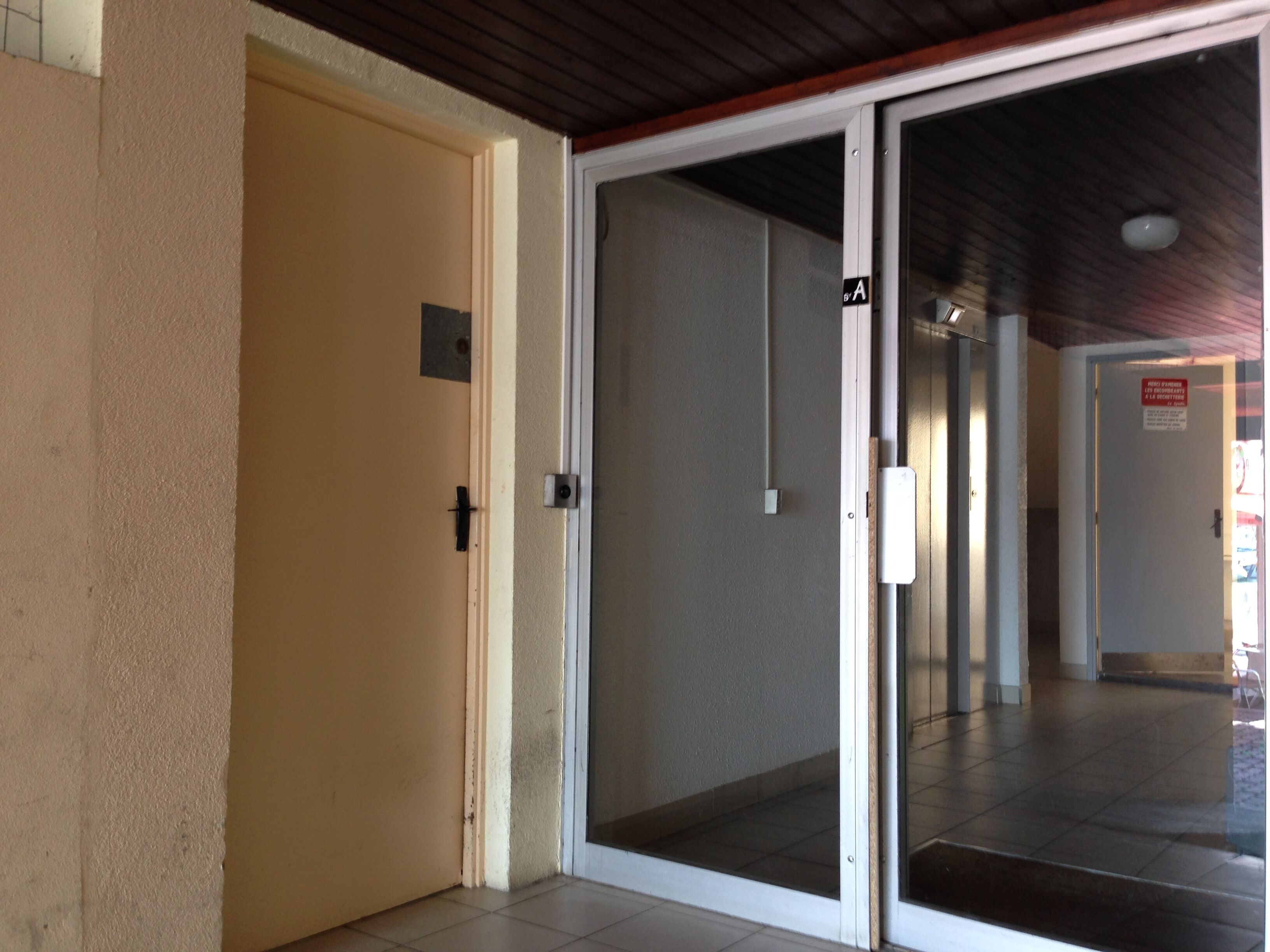Ein Hotel Eingang mit einer Schiebeglastür, einer beige farbenen Wand und einem gefliesten Boden.