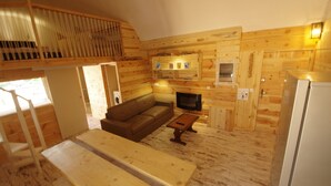 A cozy cabin interior with a wooden interior, a sofa, a table, and a fireplace.