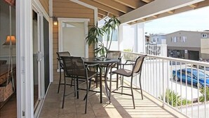 A balcony with a table and chairs, a potted plant, and a view of a residential area with houses and a parked car.