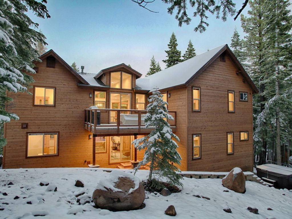 Une cabane en bois à deux étages, dotée d’un balcon et entourée d’arbres couverts de neige.