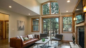 A spacious living room with a leather sofa, a coffee table, and two armchairs. Large windows offer a view of the surrounding forest. - ⭐️Luxury newly built with Sauna, Steam and Hot Tub  (Truckee)