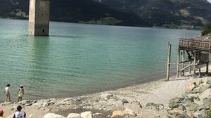 Una torre junto a un lago con costas rocosas y montañas al fondo.