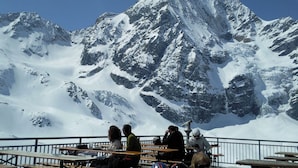 Un grupo de personas sentadas en mesas de madera con una montaña nevada al fondo.