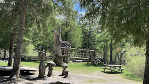 A naturalistic park area with wooden structures, a picnic table, and a small clearing surrounded by trees.
