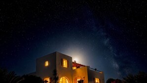 Una casa bajo un cielo iluminado por la luna, un muro de piedra y una vista despejada de las estrellas.