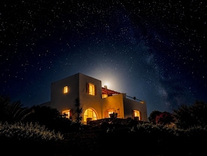 Une maison sous un ciel illuminé par la lune, avec un mur de pierre et une vue dégagée sur les étoiles.
