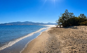 A beach with clear water, distant mountains, and a few people sitting on the sand. - Hilltop Home Sea Views & Terrace Dining near Aliki (ageria)